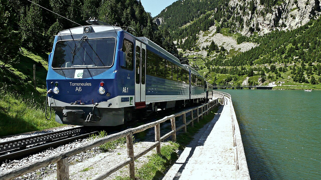 El Tren Cremallera de la Vall de Núria circulando junto al embalse en la Vall de Núria - By Alberto-g-rovi - Own work, CC BY-SA 3.0, https://commons.wikimedia.org/w/index.php?curid=26966978.
